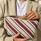 Woman holding the burgundy striped makeup bag open with a perfume bottle inside