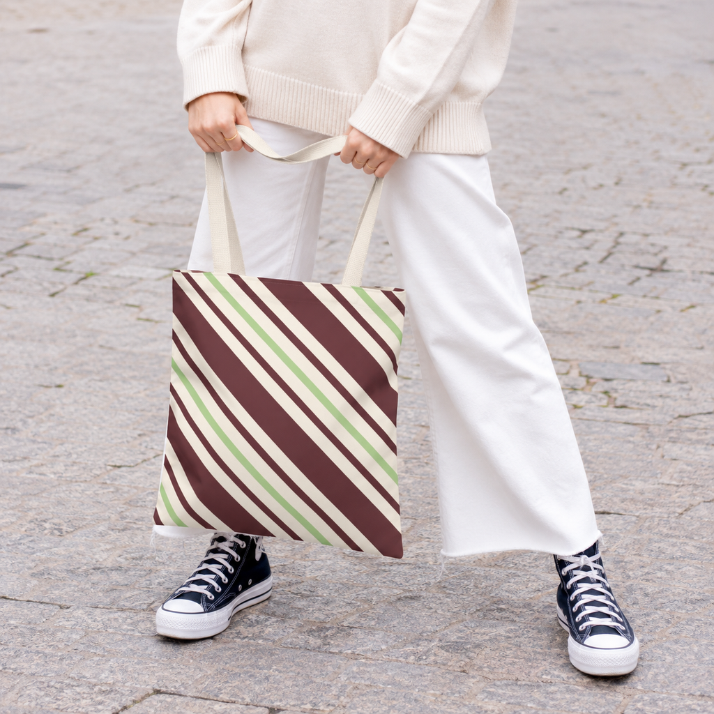 Woman in white trousers and sneakers holding the burgundy diagonal striped tote bag
