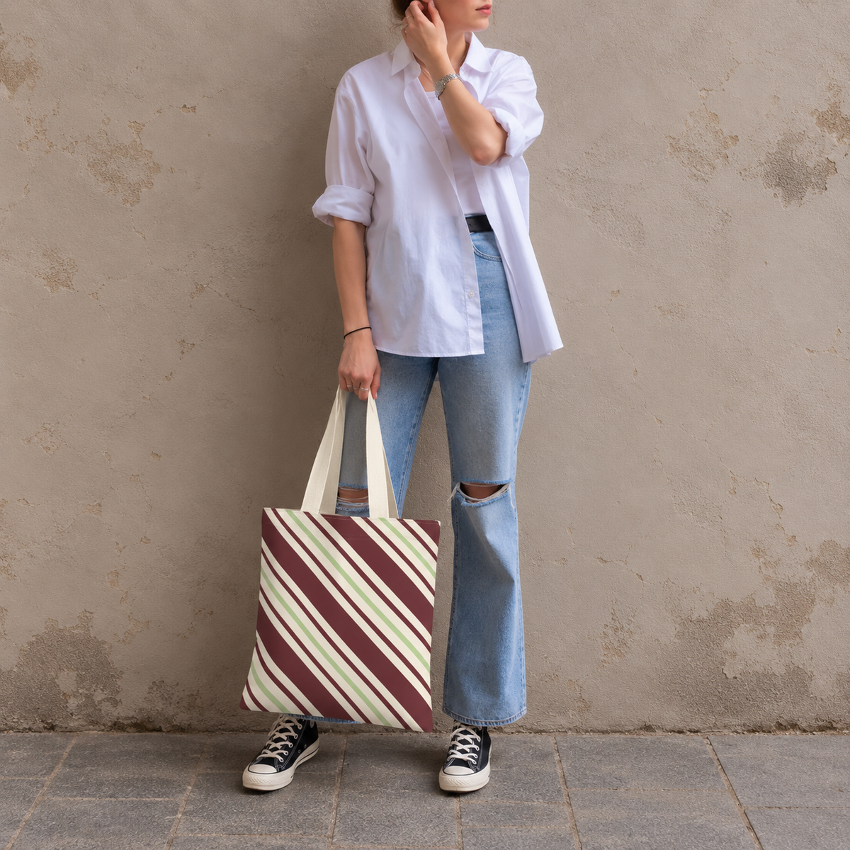 Woman in a white shirt and jeans holding the burgundy green diagonal striped tote bag