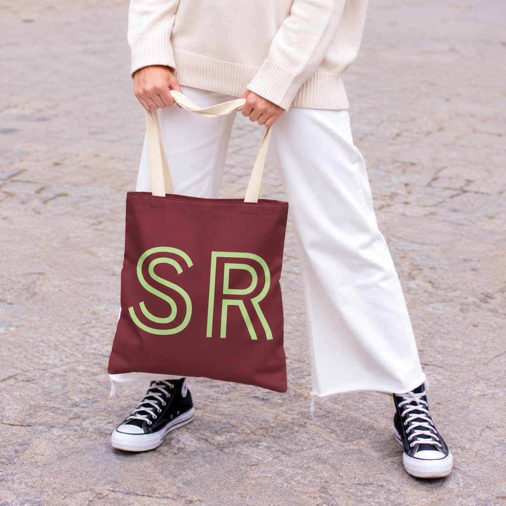 Model holding the Burgundy Green Monogram personalized tote bag in front of white trousers