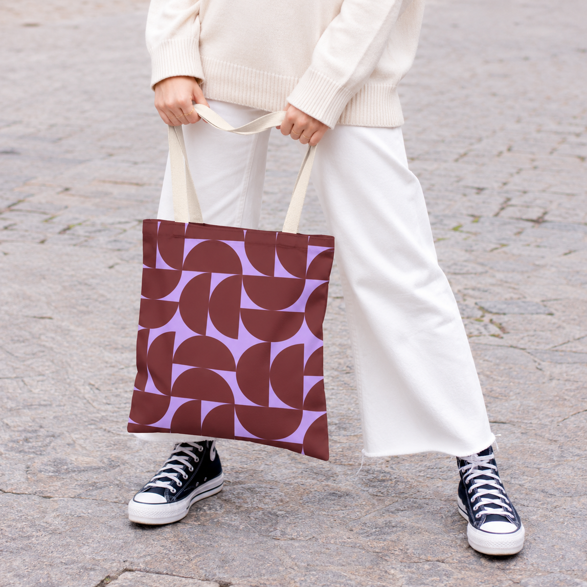 Model holding the burgundy lilac half circle tote bag in front of white trousers