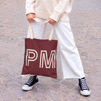 Woman in white trousers and sneakers holding the burgundy monogram personalized tote bag