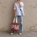 Woman in a white shirt and jeans holding the burgundy monogram personalized tote bag