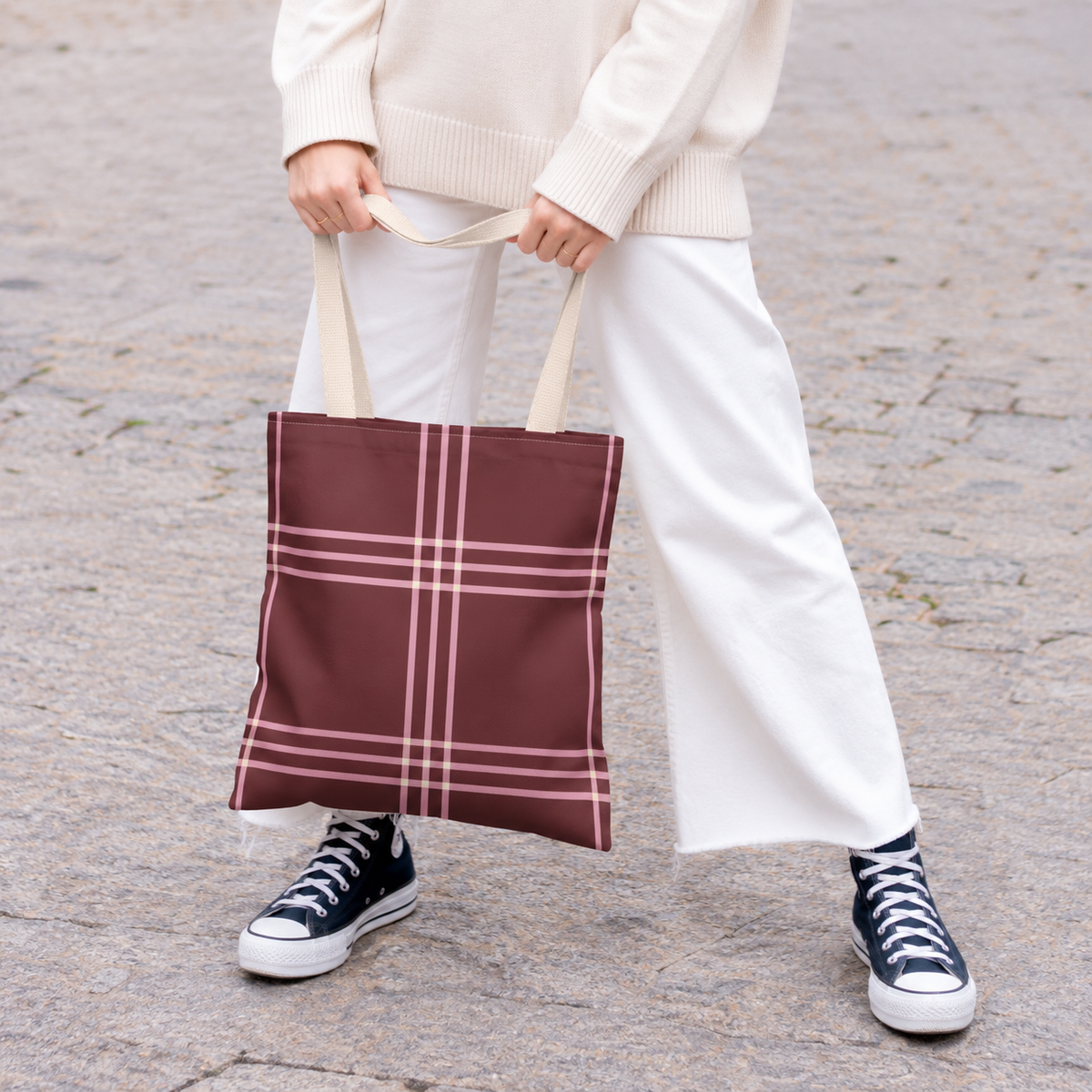 Model holding the burgundy pink plaid tote bag in front of white trousers