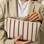 Hands holding the open burgundy pinstripe makeup bag