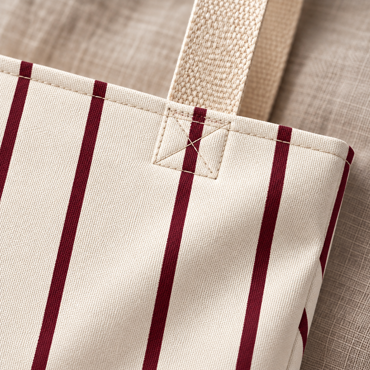 Close-up of the thin burgundy pinstripes on cream and the beige handle of the pinstripe tote bag