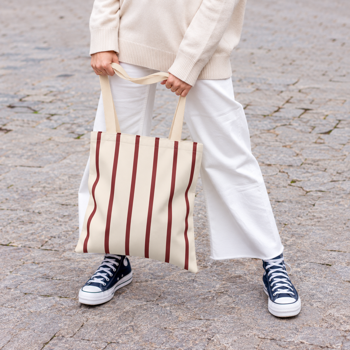Woman in white trousers holding the burgundy pinstripe tote bag by its handles