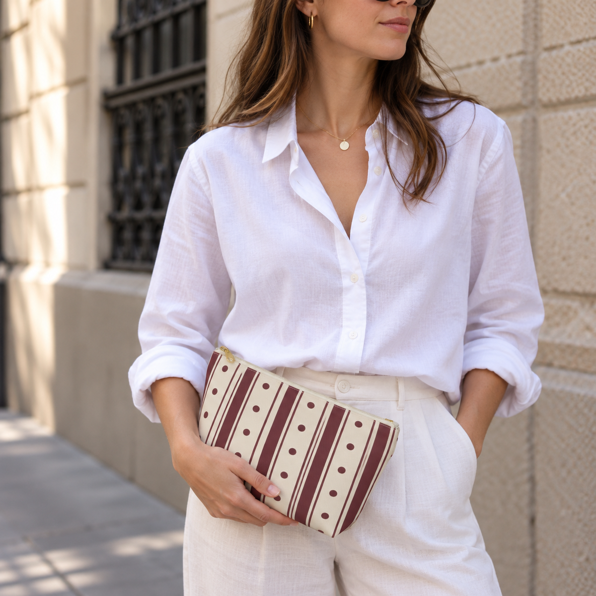 Woman in a white shirt holding the burgundy polka dot striped makeup bag as a clutch