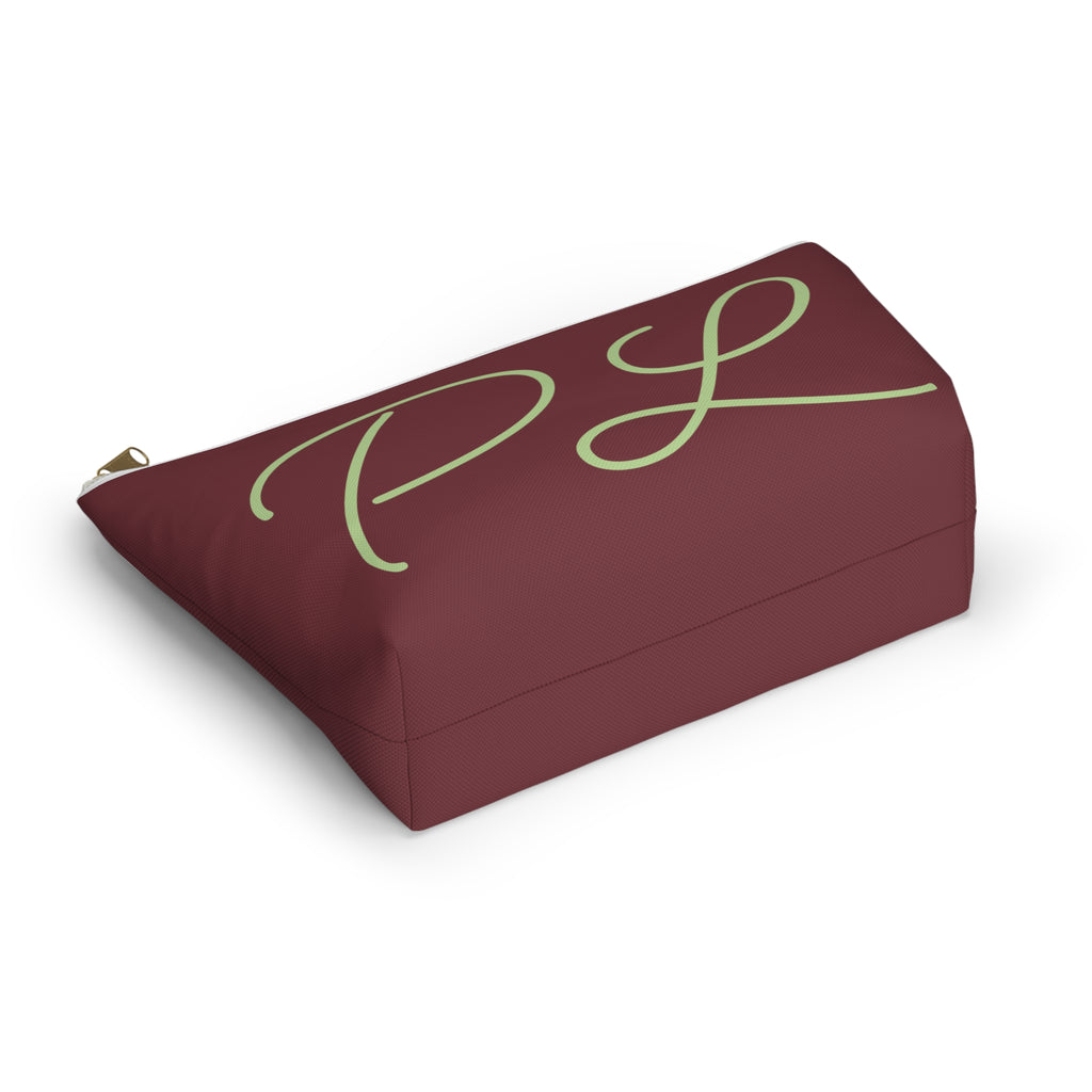 Burgundy personalized makeup bag lying on its side with green script initials
