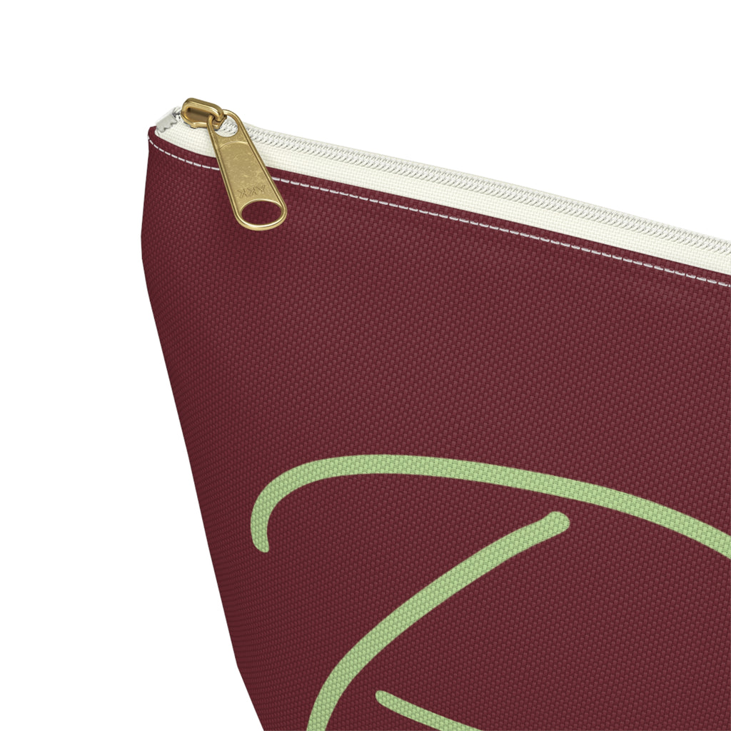 Close-up of the gold zipper pull and green script lettering on the burgundy makeup bag