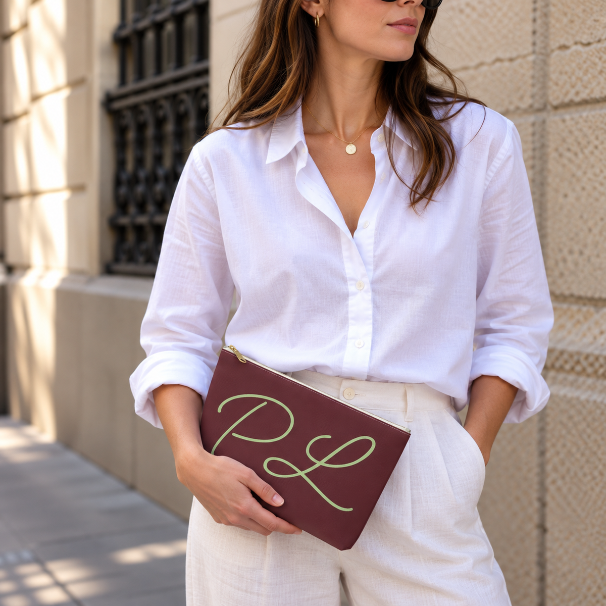 Model in a white shirt holding the burgundy monogram makeup bag at her waist