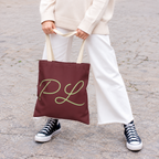 Model in white trousers holding the burgundy personalized tote bag with green script initials