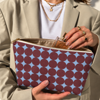 Hands holding the open Burgundy Sky Blue Geometric makeup bag filled with cosmetics