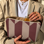 Model in a beige blazer taking a product out of the open burgundy taupe geometric makeup bag
