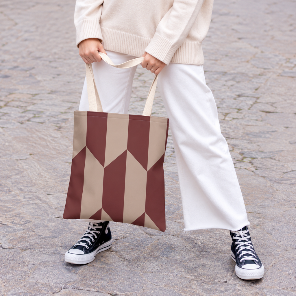 Model holding the burgundy taupe geometric tote bag in front of white trousers
