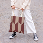 Model holding the burgundy taupe geometric tote bag in front of white trousers
