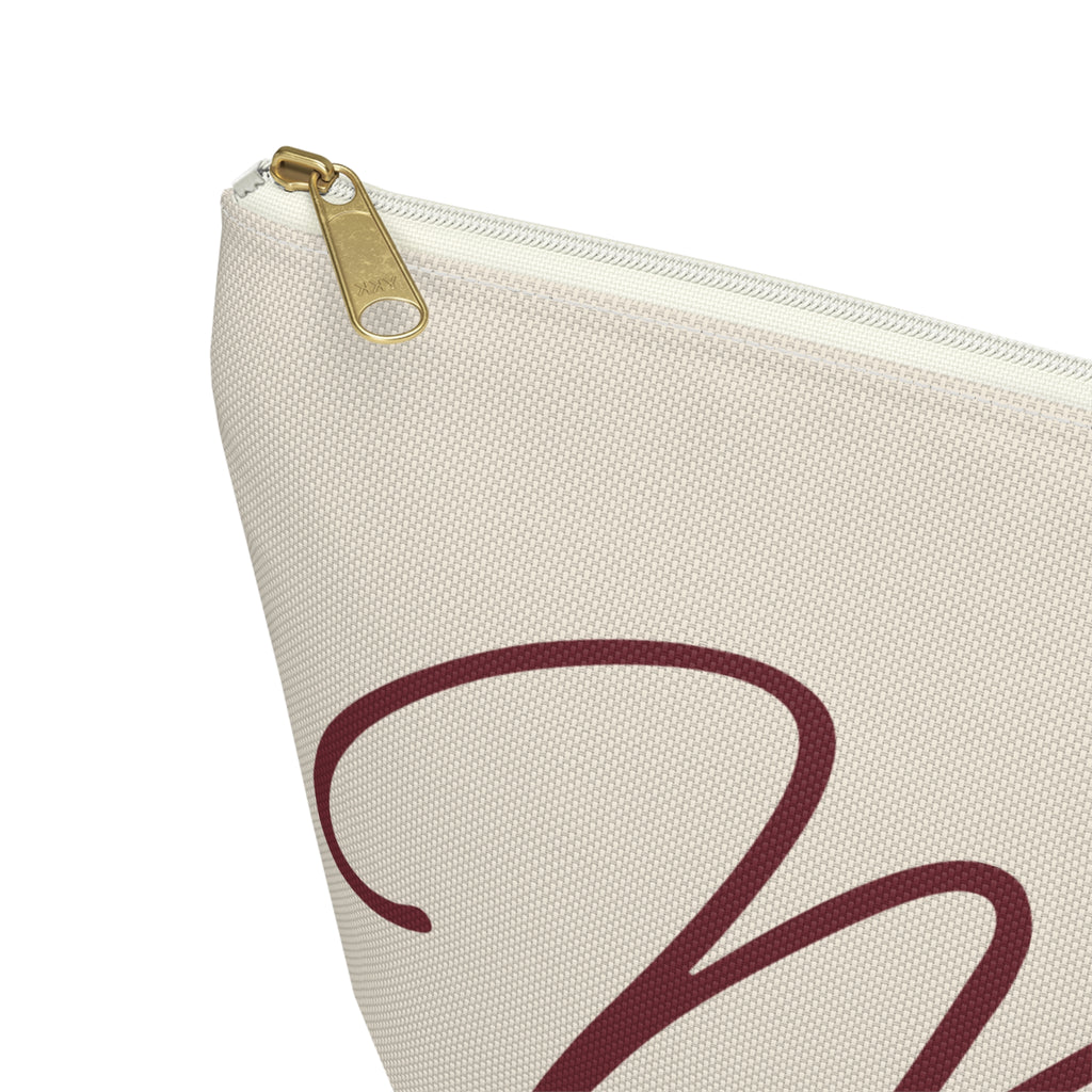 Close-up of the gold zipper pull and burgundy script lettering on the cream makeup bag