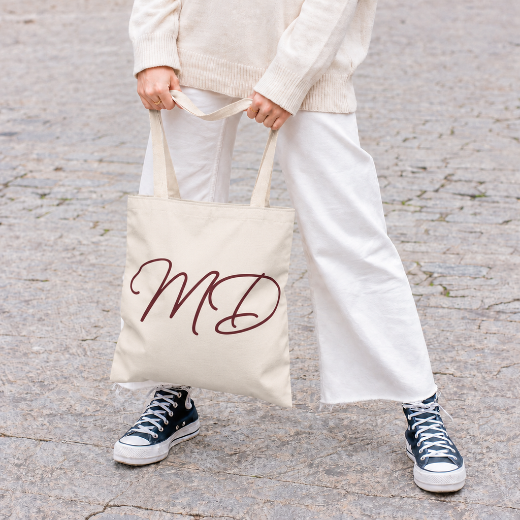 Model in white trousers holding the cream personalized tote bag with burgundy script initials