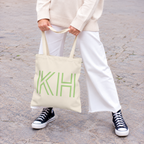 Model holding the Cream Green Monogram personalized tote bag in front of white trousers
