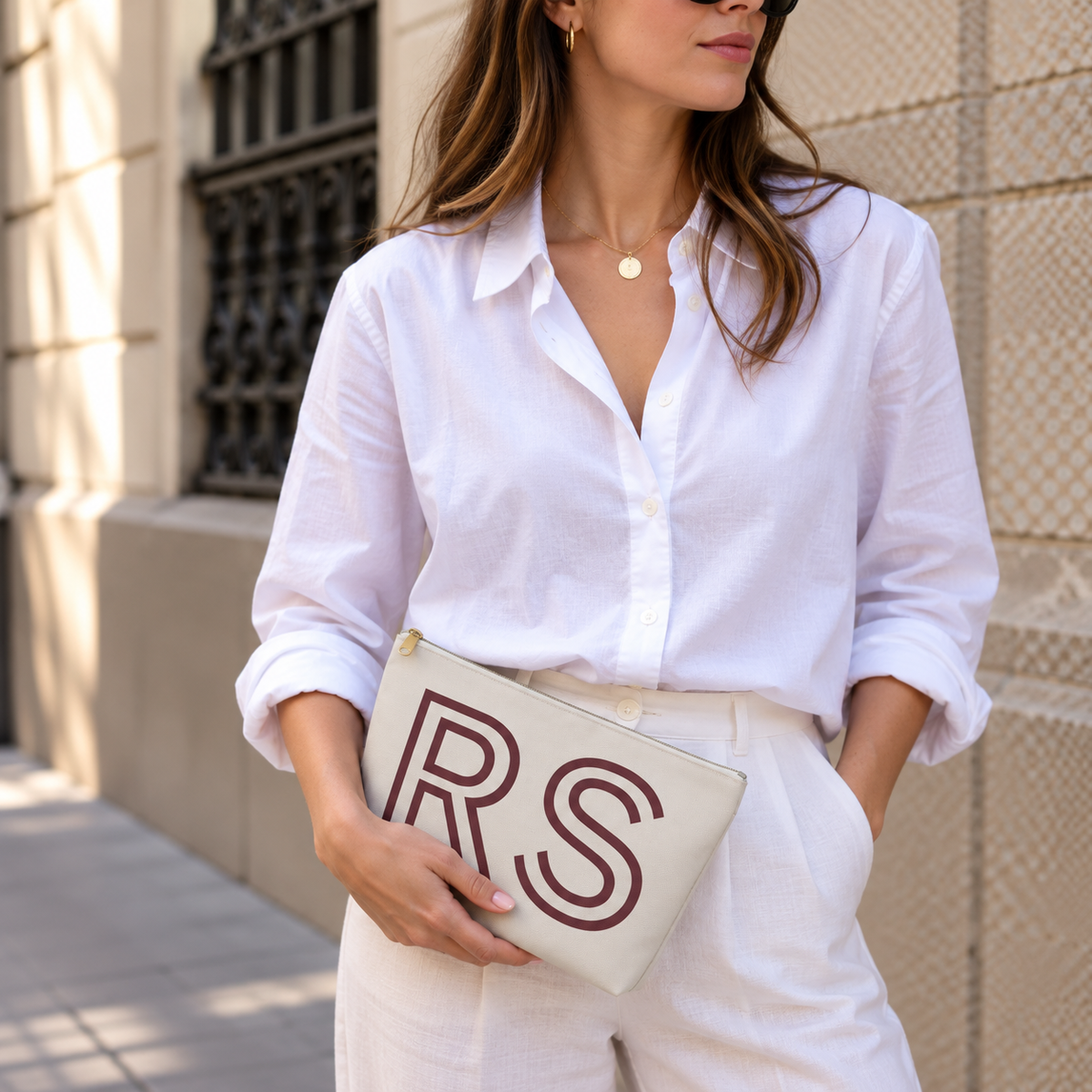 Woman in a white shirt holding the cream RS personalized makeup bag as a clutch