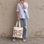 Woman in a white shirt and jeans holding the cream RS monogram personalized tote bag