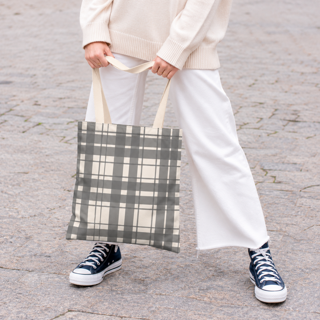 Woman in white trousers holding the gray cream plaid tote bag by the handles