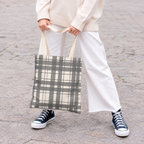 Woman in white trousers holding the gray cream plaid tote bag by the handles