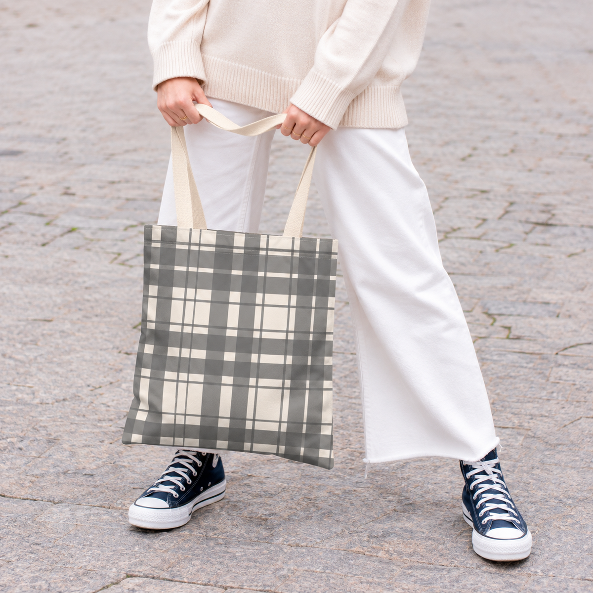 Woman in white trousers holding the gray cream plaid tote bag by the handles