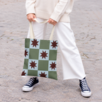 Model holding the green blue star checkered tote bag in front of white trousers