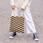 Woman in white trousers holding the green burgundy checkered tote bag by the handles