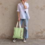 Model standing outdoors with the Green Burgundy Name personalized tote bag in a full-body photo