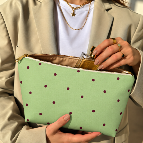 Hands holding the green polka dot makeup bag with a perfume bottle inside