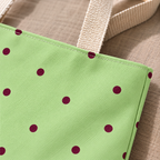Close-up of burgundy polka dots on sage green next to the beige tote handle