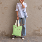 Woman in jeans and sneakers holding the green burgundy polka dot tote bag