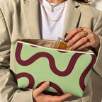 Woman holding the green burgundy wavy line makeup bag open with the gold zipper