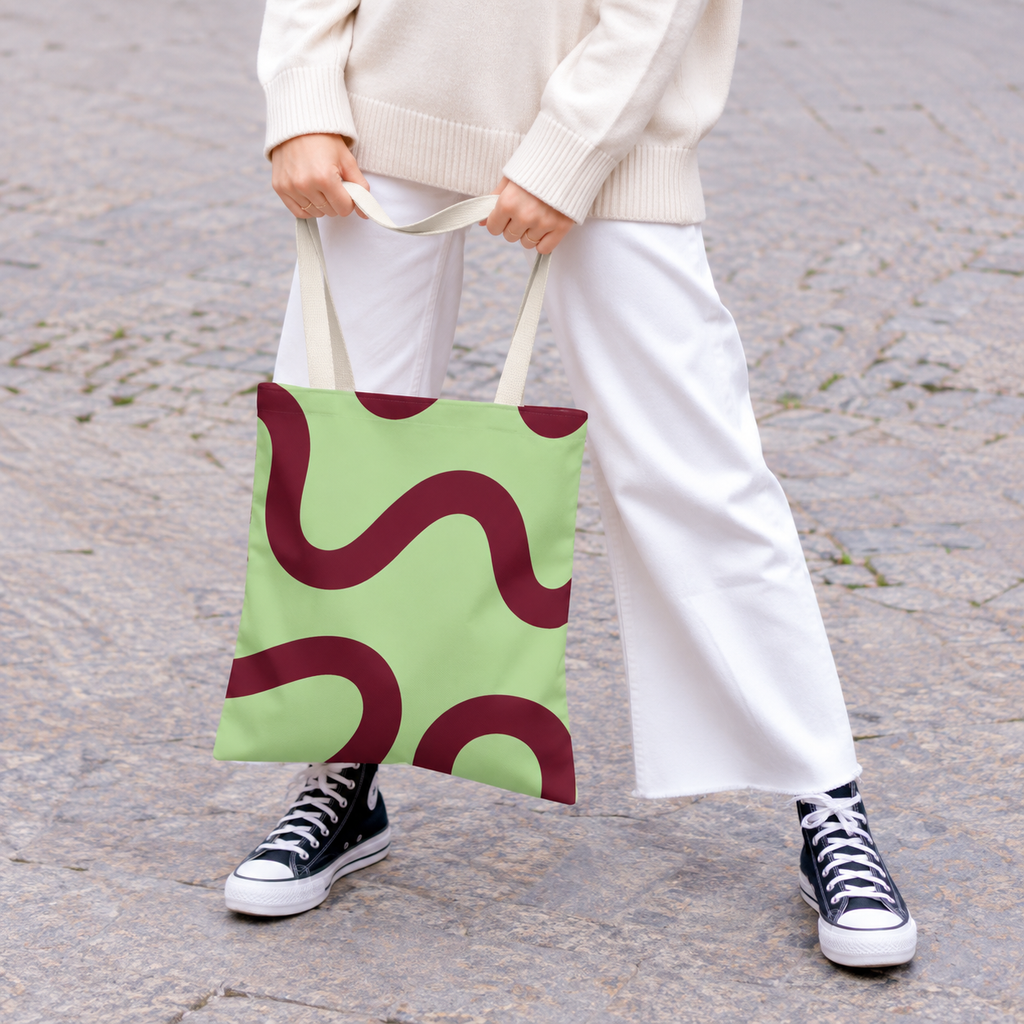 Woman in white trousers holding the green burgundy wavy line tote bag by the handles