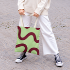 Woman in white trousers holding the green burgundy wavy line tote bag by the handles