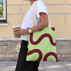 Woman carrying the green burgundy wavy line tote bag on her shoulder while holding a drink
