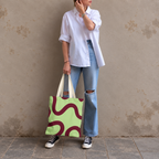 Woman standing in jeans and a white shirt with the green burgundy wavy line tote bag