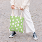 Model in white trousers holding the green daisy floral tote bag