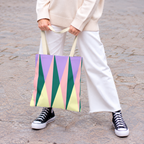Model in white trousers holding the green pink triangle tote bag
