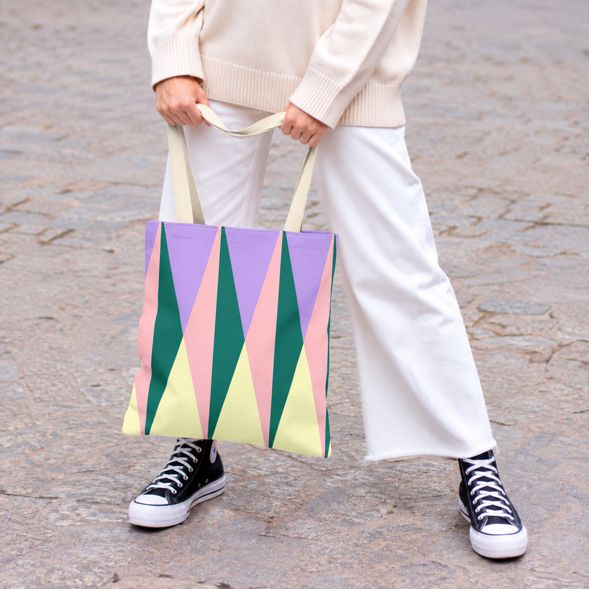Model in white trousers holding the green pink triangle tote bag