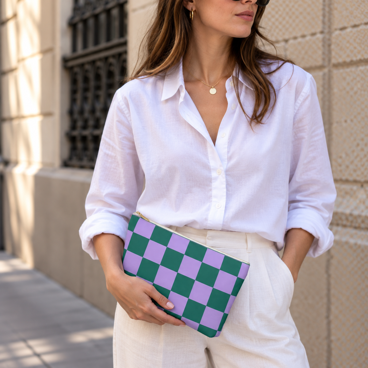 Woman in a white shirt holding the green purple checkered makeup bag as a clutch