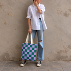 Woman standing in jeans and a white shirt with the green purple checkered tote bag