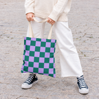 Woman in white trousers holding the green purple checkered tote bag by the handles