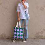 Woman in jeans and sneakers holding the green purple diamond checkered tote bag
