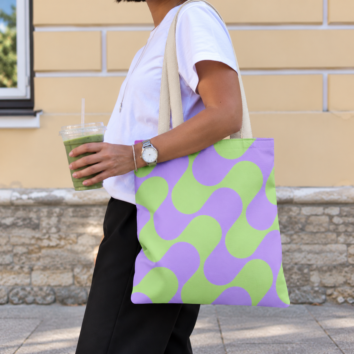 Woman carrying the green purple geometric tote bag on her shoulder while holding a drink