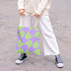 Woman in white trousers holding the green purple geometric tote bag by the handles