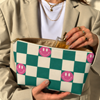 Hands holding the open green smiley checkered makeup bag with a perfume bottle inside