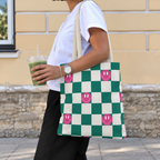 Woman with an iced drink wearing the green smiley checkered tote bag